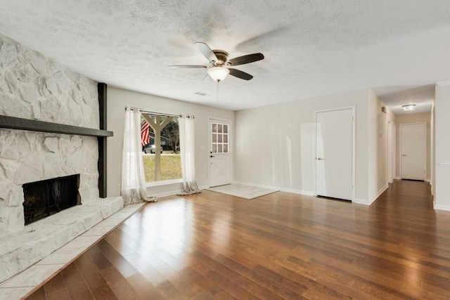 unfurnished living room with a textured ceiling, wood finished floors, a fireplace, baseboards, and ceiling fan