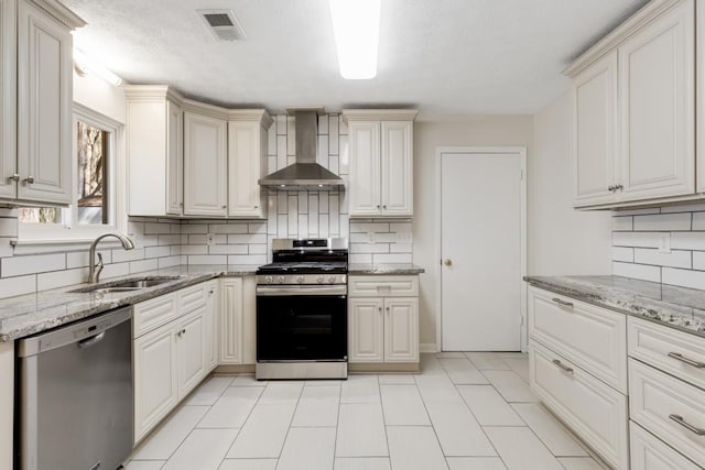 kitchen with visible vents, a sink, stainless steel appliances, wall chimney range hood, and light stone countertops