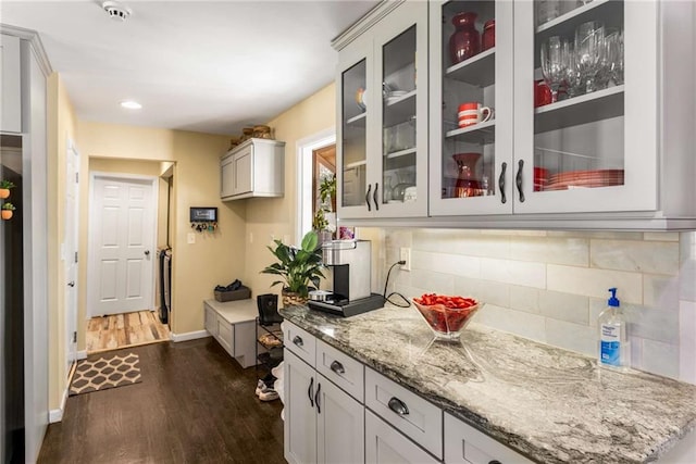 kitchen featuring light stone counters, tasteful backsplash, dark wood-style flooring, and glass insert cabinets