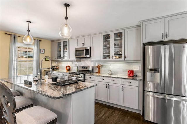 kitchen featuring stone counters, dark wood finished floors, backsplash, appliances with stainless steel finishes, and a kitchen bar