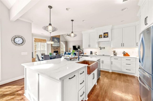 kitchen featuring sink, white cabinetry, stainless steel appliances, light stone countertops, and a kitchen island with sink