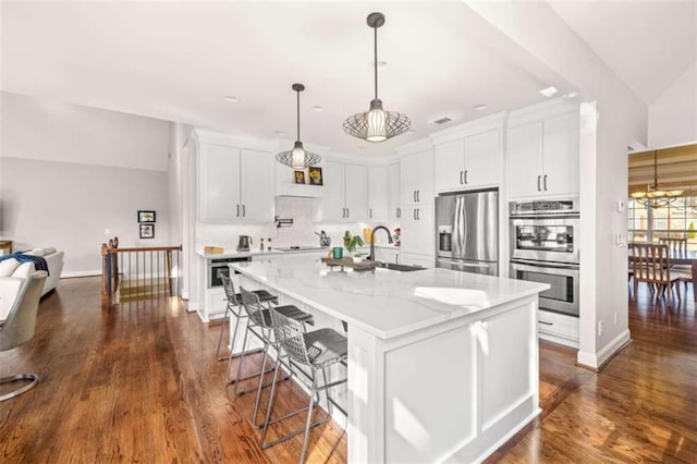 kitchen with appliances with stainless steel finishes, sink, white cabinets, a kitchen island with sink, and light stone countertops