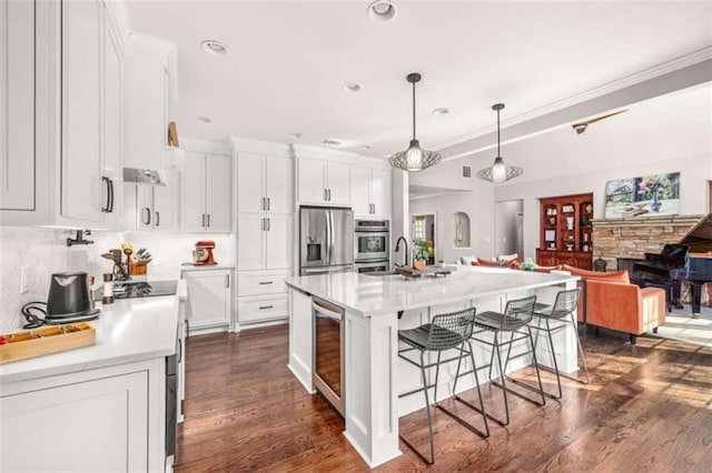 kitchen featuring a breakfast bar, appliances with stainless steel finishes, hanging light fixtures, wine cooler, and an island with sink