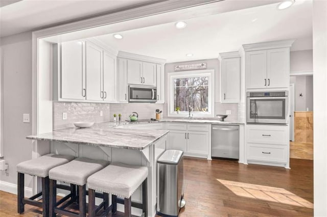 kitchen featuring a breakfast bar, white cabinets, kitchen peninsula, stainless steel appliances, and light stone countertops