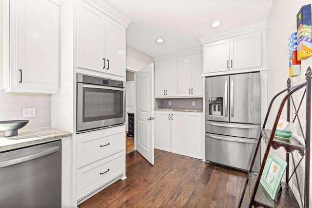 kitchen featuring dark wood-type flooring, appliances with stainless steel finishes, white cabinetry, light stone counters, and decorative backsplash