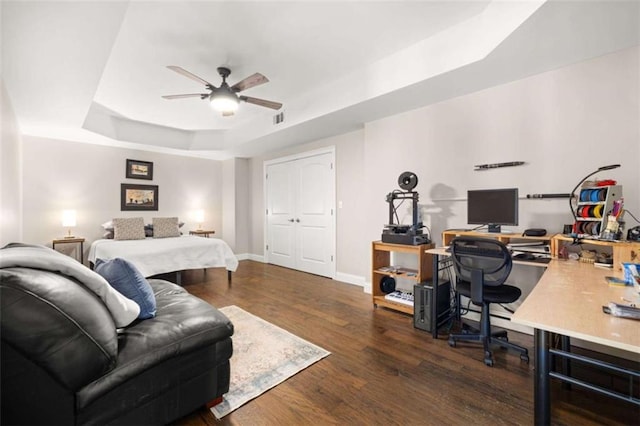 bedroom featuring a raised ceiling, dark wood-type flooring, and ceiling fan