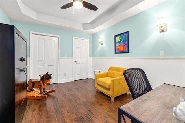 office space featuring dark hardwood / wood-style flooring, a tray ceiling, and ceiling fan