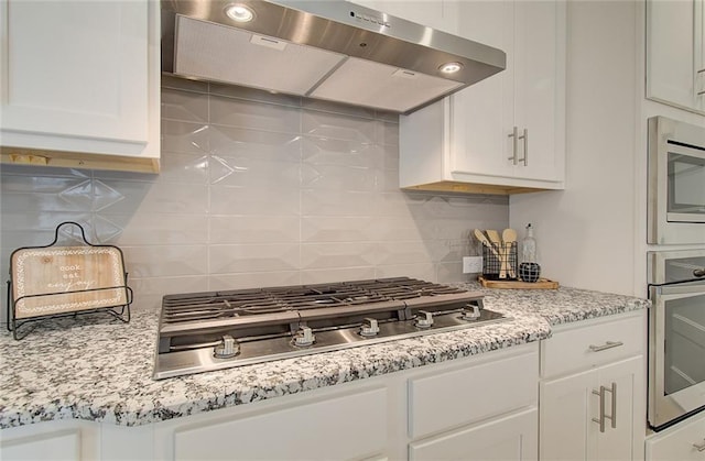 kitchen featuring tasteful backsplash, white cabinets, appliances with stainless steel finishes, light stone countertops, and under cabinet range hood