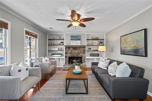 living area with crown molding, visible vents, wood finished floors, and a stone fireplace