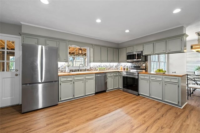 kitchen featuring light wood-style flooring, appliances with stainless steel finishes, a sink, light countertops, and backsplash