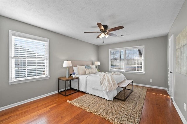 bedroom featuring a ceiling fan, a textured ceiling, baseboards, and wood finished floors