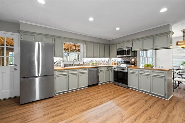 kitchen featuring stainless steel appliances, tasteful backsplash, light countertops, light wood-style flooring, and a sink