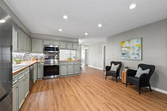 kitchen featuring light countertops, appliances with stainless steel finishes, gray cabinets, light wood finished floors, and tasteful backsplash