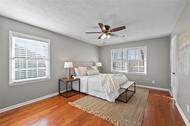 bedroom with a textured ceiling, wood finished floors, and baseboards