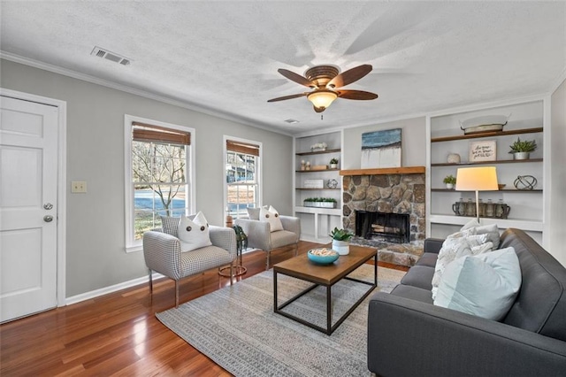 living room featuring a textured ceiling, a stone fireplace, wood finished floors, visible vents, and baseboards