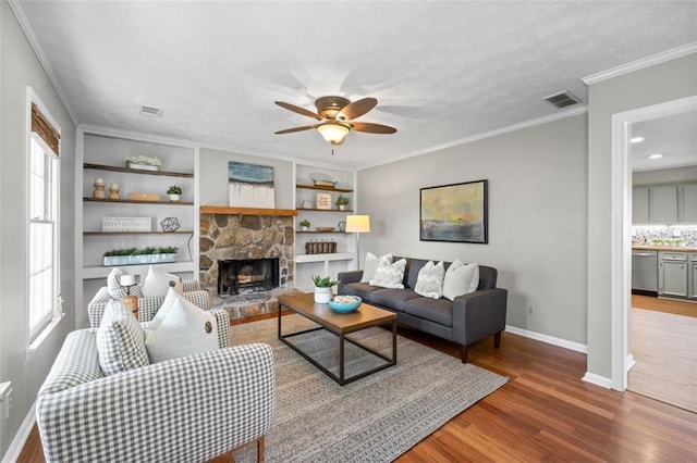 living room featuring a stone fireplace, wood finished floors, visible vents, baseboards, and crown molding