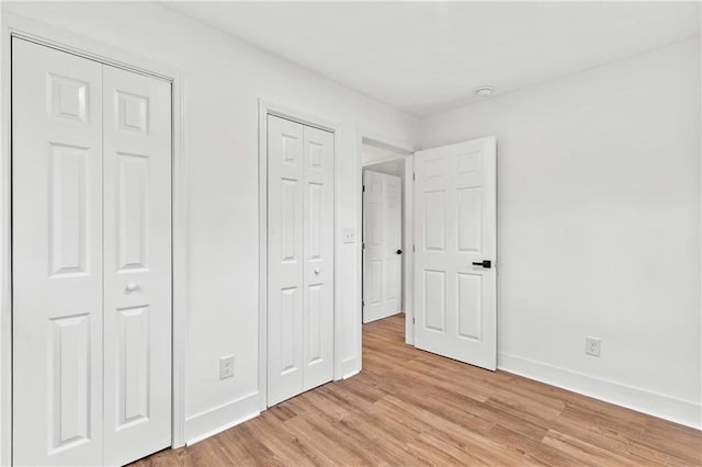 unfurnished bedroom with light hardwood / wood-style floors and multiple closets