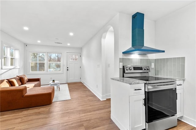 kitchen with stainless steel range with electric stovetop, backsplash, wall chimney exhaust hood, light hardwood / wood-style floors, and white cabinetry