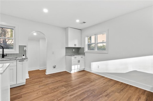 kitchen featuring white cabinetry, sink, light stone counters, backsplash, and light hardwood / wood-style floors