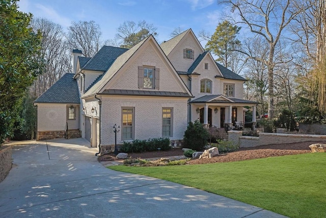 view of front facade with brick siding, a chimney, concrete driveway, a front yard, and a standing seam roof