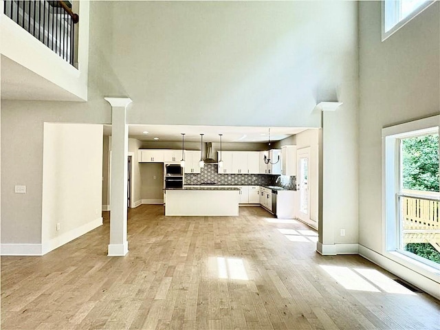 237 Lotus Ln, Covington, GA 30016 - unfurnished living room featuring a high ceiling, light wood-style flooring, decorative columns, and recessed lighting