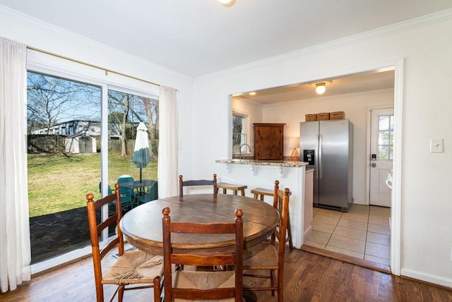 dining space featuring light wood-type flooring, crown molding, and baseboards