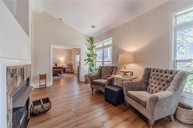 sitting room with plenty of natural light, a tile fireplace, wood finished floors, lofted ceiling, and baseboards