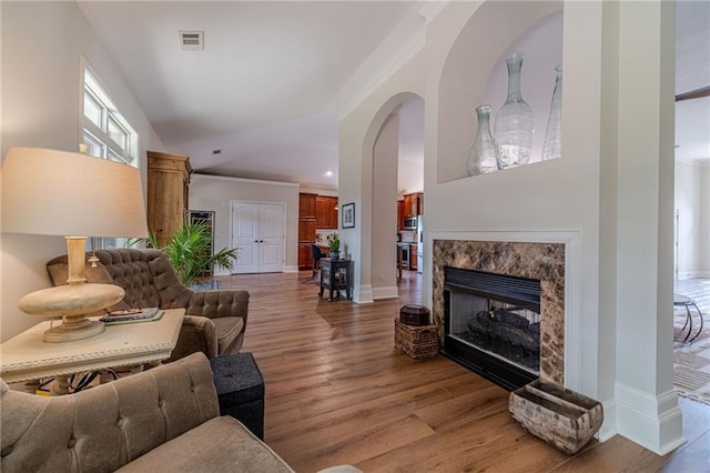 living area featuring ornamental molding, light wood-style floors, a premium fireplace, baseboards, and arched walkways
