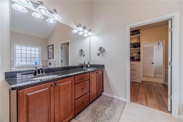 full bath with vaulted ceiling, double vanity, a walk in closet, tile patterned flooring, and baseboards