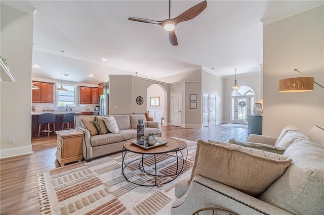 living area with arched walkways, crown molding, ceiling fan, baseboards, and light wood-type flooring