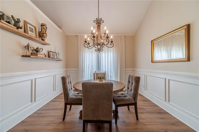 dining space featuring a chandelier, a decorative wall, wood finished floors, wainscoting, and lofted ceiling