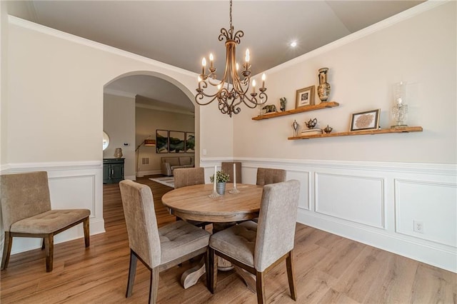 dining area featuring light wood-style flooring, arched walkways, ornamental molding, a decorative wall, and a wainscoted wall