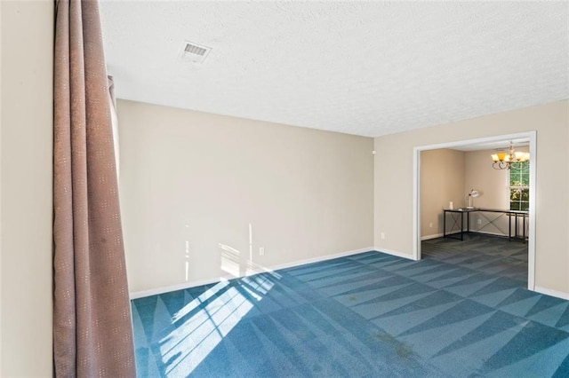 carpeted empty room featuring a textured ceiling and an inviting chandelier