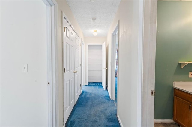 hallway with a textured ceiling and dark colored carpet