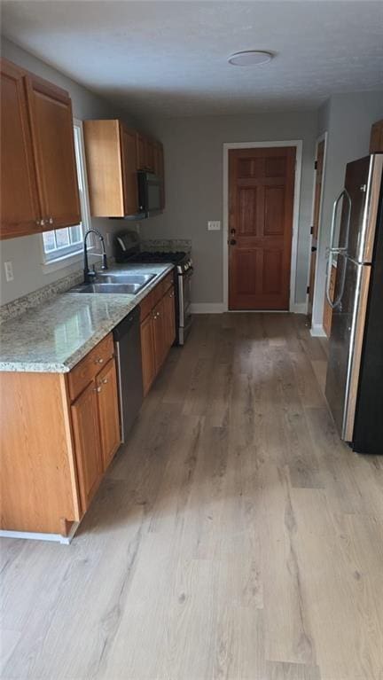 kitchen featuring baseboards, stainless steel appliances, a sink, and light wood-style floors