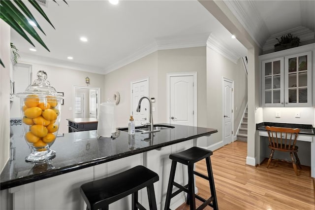 kitchen with a sink, a kitchen breakfast bar, light wood-style floors, glass insert cabinets, and crown molding