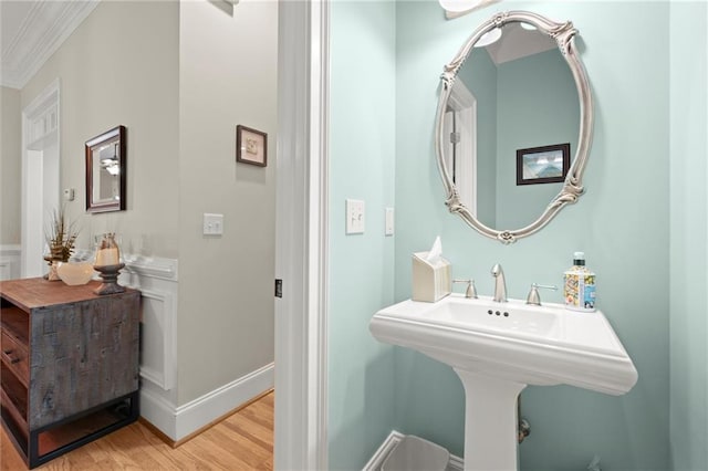 bathroom featuring a sink, crown molding, baseboards, and wood finished floors