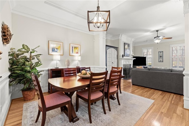 dining room featuring decorative columns, ornamental molding, light wood-style floors, a fireplace, and ceiling fan with notable chandelier