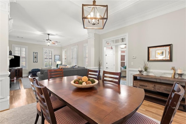 dining room with crown molding, light wood-style floors, wainscoting, ornate columns, and ceiling fan with notable chandelier