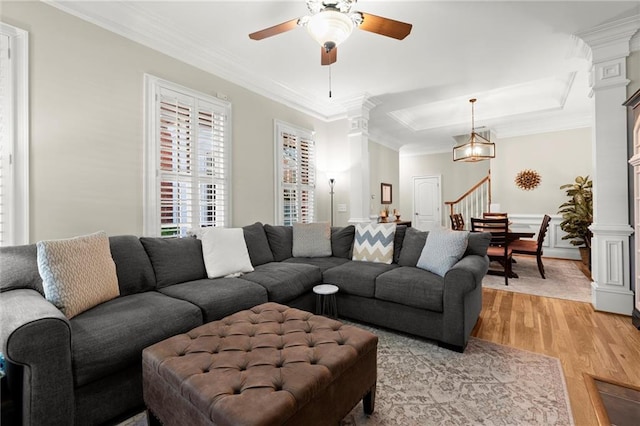 living area featuring ornate columns, light wood finished floors, stairway, and crown molding