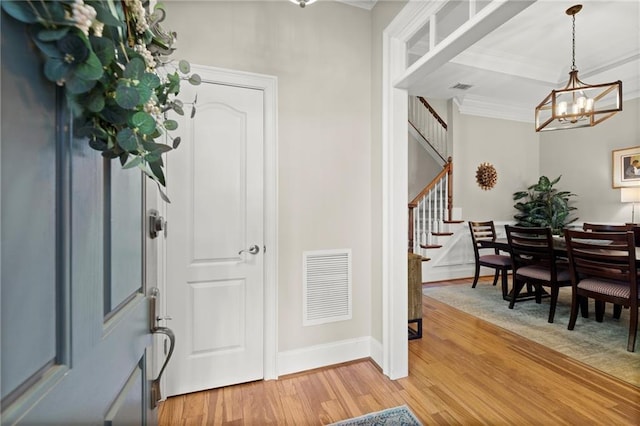 entryway with light wood-style floors, stairs, visible vents, and ornamental molding