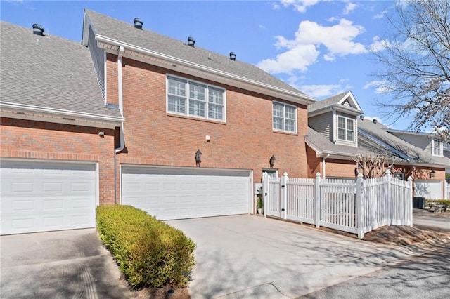 exterior space with brick siding, a shingled roof, an attached garage, fence, and driveway