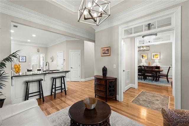 living area featuring light wood-style flooring, crown molding, baseboards, and a notable chandelier