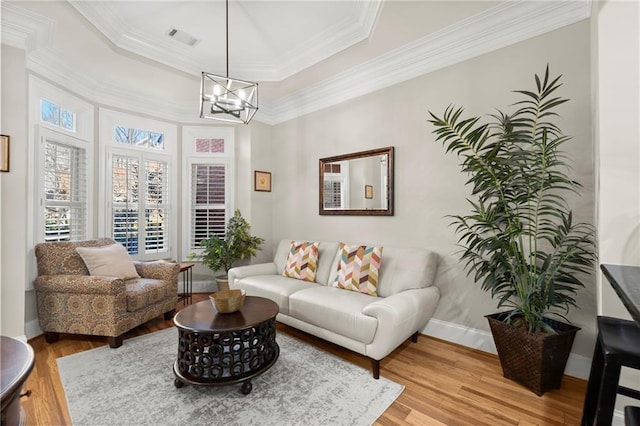 living area featuring a tray ceiling, visible vents, ornamental molding, wood finished floors, and baseboards