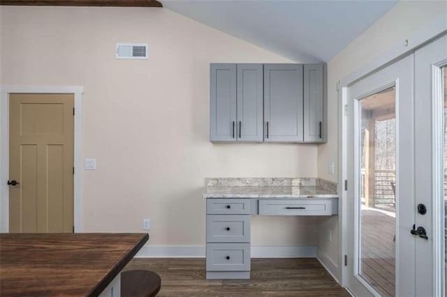 unfurnished office with vaulted ceiling, dark hardwood / wood-style floors, built in desk, and french doors