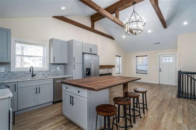 kitchen with sink, butcher block counters, hanging light fixtures, stainless steel appliances, and a center island