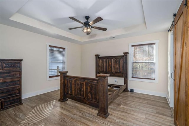 bedroom with multiple windows, a tray ceiling, a barn door, and light wood-type flooring