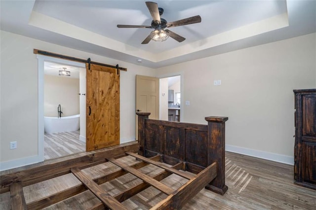 bedroom featuring a raised ceiling, ceiling fan, a barn door, and dark hardwood / wood-style flooring