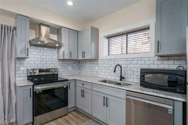 kitchen featuring wall chimney range hood, sink, appliances with stainless steel finishes, gray cabinetry, and light stone countertops