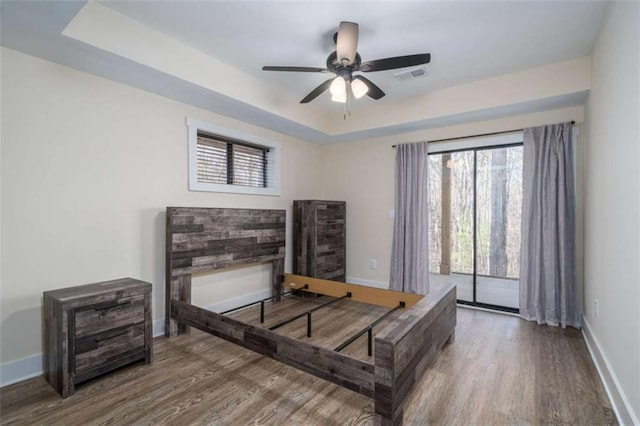 bedroom with hardwood / wood-style flooring, access to outside, and a tray ceiling